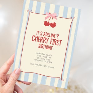 Op de afbeelding: Een rechthoekige uitnodigingskaart met een lichtblauwe en crèmekleurige gestreepte achtergrond. De kaart bevat de tekst "IT'S ADELINE'S CHERRY FIRST BIRTHDAY" in het rood, samen met evenementdetails en een kersengrafiek. De kaart wordt door een hand vastgehouden.