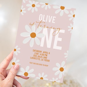 May include: Pink birthday invitation with a white daisy pattern. The text reads "Olive is turning one" with a large white "one" in the center. The invitation includes the date, time, address, and RSVP information.