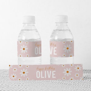 May include: Two clear plastic water bottles with pink and white daisy patterned labels that say "Happy Birthday Olive". There is also a matching label with the same pattern that says "Happy Birthday Olive".