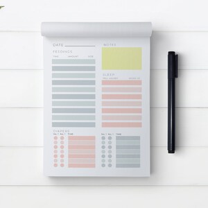 Op de afbeelding: Een wit, printbaar baby-trackerblad met secties voor datum, voedingen, slaap, luiers en notities. Het blad heeft een geel notitiegedeelte en een zwarte pen.