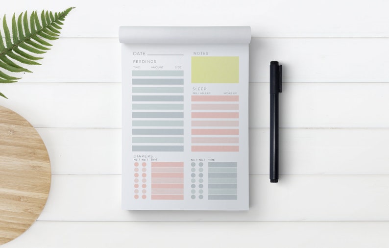 Op de afbeelding: Een wit, printbaar baby-trackerblad met secties voor datum, voedingen, slaap, luiers en notities. Het blad heeft een geel notitiegedeelte en een zwarte pen.