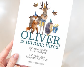 Può includere: Un invito di compleanno per un bambino di nome Oliver che compie tre anni. L'invito presenta un'illustrazione ad acquerello di un cervo, una volpe e un riccio che indossano cappelli da festa e tengono dei regali. Il testo "OLIVER is turning three!" è in un carattere blu-verde. L'invito include la data, l'ora, l'indirizzo e le informazioni RSVP.