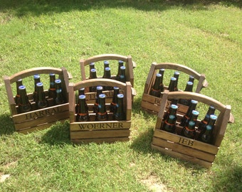 May include: Four wooden beer carriers with handles. Each carrier holds six bottles of beer and has a name on the front: Harral, Woerner, Bob, and Jeb.
