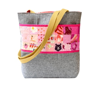 Peut inclure: Un sac cabas gris avec un panneau de tissu patchwork rose et blanc sur le devant. Le sac a deux anses jaunes.