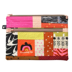 Puede incluir: Una bolsa de doble cremallera de patchwork con un dise&ntilde;o acolchado. La bolsa est&aacute; hecha de varias telas con diferentes patrones, incluyendo estrellas, p&aacute;jaros, flores y un arco&iacute;ris. La bolsa tiene una cremallera marr&oacute;n y el texto "Looking Up" est&aacute; impreso en la parte delantera.