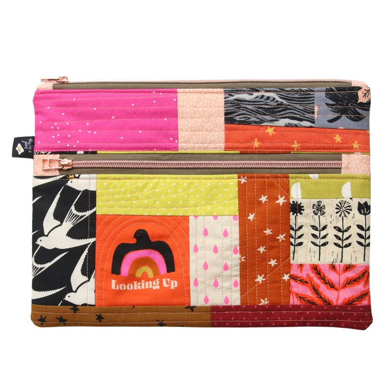 Puede incluir: Una bolsa de doble cremallera de patchwork con un dise&ntilde;o acolchado. La bolsa est&aacute; hecha de varias telas con diferentes patrones, incluyendo estrellas, p&aacute;jaros, flores y un arco&iacute;ris. La bolsa tiene una cremallera marr&oacute;n y el texto "Looking Up" est&aacute; impreso en la parte delantera.