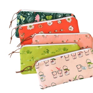 May include: Five zippered pouches with different floral and nature-themed prints. The pouches are stacked on top of each other, with the top pouch being green and the bottom pouch being pink. The pouches are all made of fabric and have a white zipper.