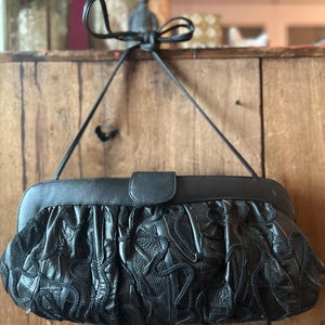 May include: A black leather clutch bag with a decorative woven design. The bag has a flap closure and a long strap.
