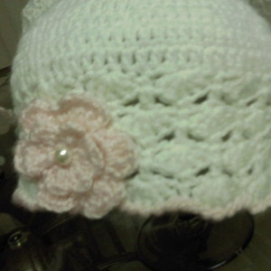 May include: White crocheted hat with a pink crocheted flower and a pearl accent.