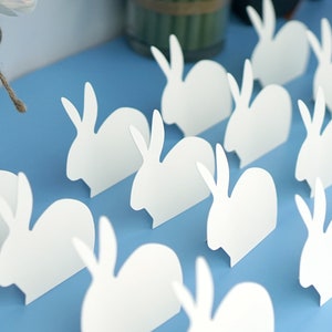 Peut inclure: Une collection de découpes de lapins en papier blanc sur un fond bleu clair. Les lapins sont disposés en rangées, la tête dans la même direction.