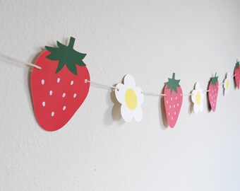 May include: A red and green strawberry and white daisy paper garland. The garland is strung on white twine.