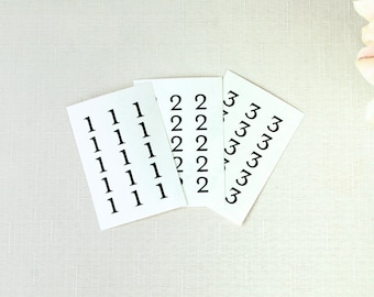 May include: Three white cards with black numbers printed on them. The cards are arranged in a fan shape. The numbers on the cards are 1, 2, and 3.