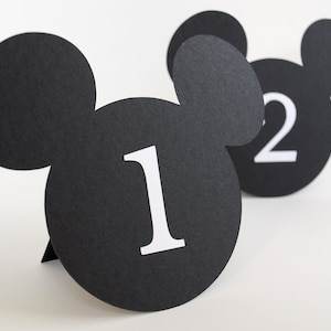 May include: Black and white Mickey Mouse-shaped table number cards with the numbers 1 and 2 printed in white.