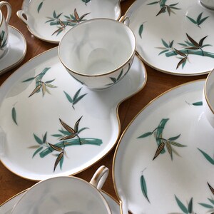 May include: A set of five white porcelain teacups and saucers with a gold rim and a green bamboo design. The saucers are slightly larger than the cups and have a scalloped edge.
