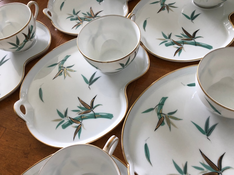 May include: A set of five white porcelain teacups and saucers with a gold rim and a green bamboo design. The saucers are slightly larger than the cups and have a scalloped edge.