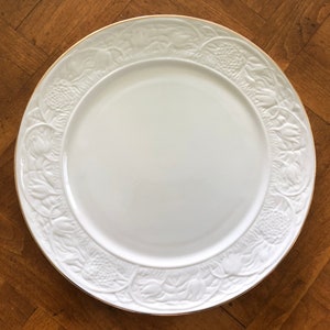 May include: White ceramic dinner plate with a raised floral design around the rim and a gold trim.