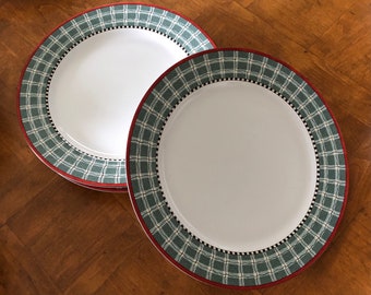 Puede incluir: Dos platos de cena de cerámica blanca con un borde de cuadros verdes y rojos. Los platos están apilados uno encima del otro.