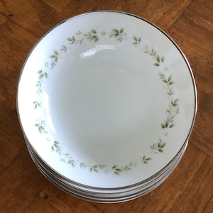 May include: A stack of white ceramic bowls with a silver rim and a floral design. The bowls have a green and white floral pattern around the rim.