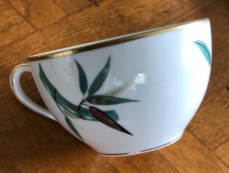 May include: A white porcelain teacup with a gold rim and a green and gold bamboo design.