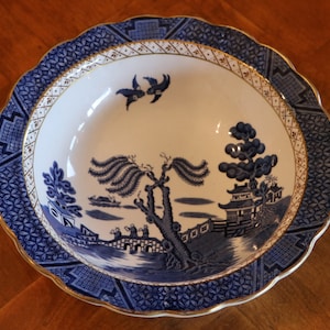 May include: A blue and white ceramic bowl with a willow pattern design. The bowl has a scalloped edge and a gold trim.