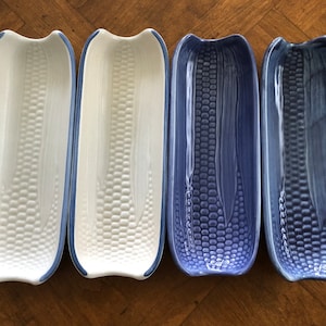 May include: Four ceramic corn on the cob serving dishes. Two are white with blue trim and two are blue with white trim.