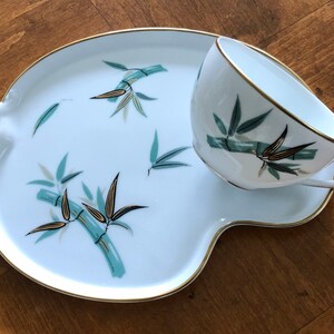 May include: A white porcelain teacup and saucer set with a gold rim and a bamboo design in shades of green and gold.