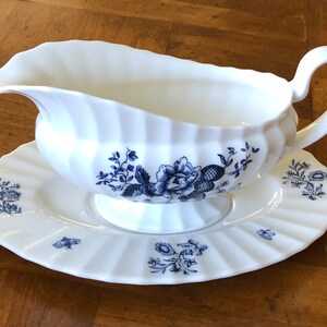May include: White porcelain gravy boat with a blue floral design and a matching saucer. The boat has a fluted edge and a handle. The saucer has a scalloped edge.