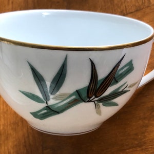 May include: A white teacup with a gold rim and a green and brown bamboo design.