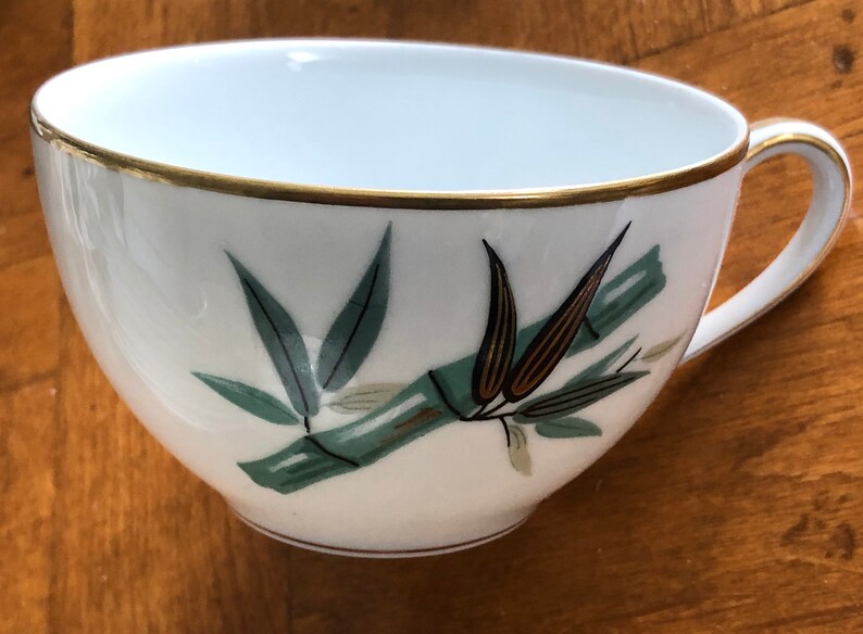 May include: A white teacup with a gold rim and a green and brown bamboo design.