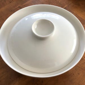 May include: A white ceramic serving dish with a smaller, round dish in the center. The dish is perfect for serving snacks or appetizers.