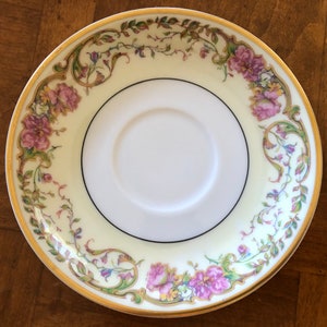 Puede incluir: Un platillo de porcelana blanca con un borde dorado y un dise&ntilde;o floral en tonos de rosa, verde y amarillo.