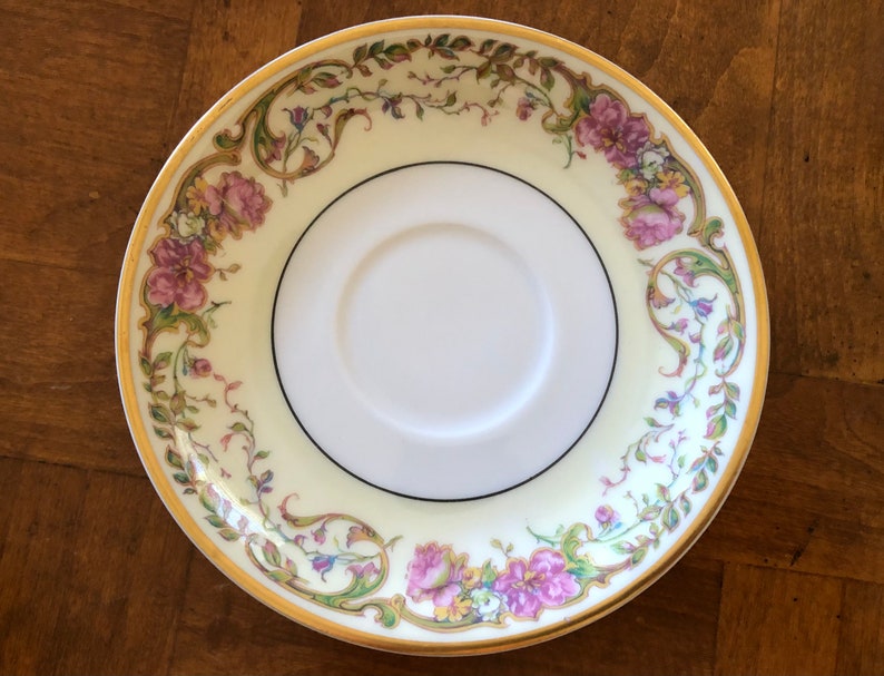Puede incluir: Un platillo de porcelana blanca con un borde dorado y un dise&ntilde;o floral en tonos de rosa, verde y amarillo.