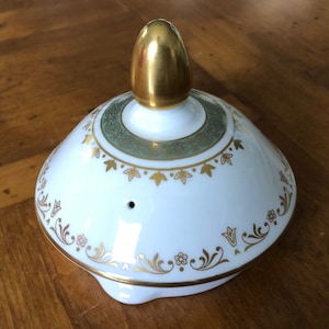 May include: White teapot lid with a gold knob and a green and gold floral design.
