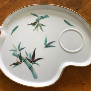 May include: White ceramic serving tray with a gold rim and a green and gold bamboo design. The tray has a small, round indentation for a cup.