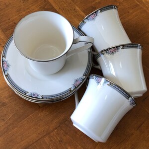 May include: Set of four white teacups and saucers with a floral design in shades of pink, blue, and gold. The cups and saucers have a delicate, feminine look.