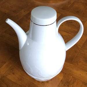 May include: White ceramic pitcher with a spout and a handle. The pitcher has a thin gold band around the top.