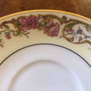 Puede incluir: Un platillo de porcelana blanca con un borde dorado y un dise&ntilde;o floral en tonos de rosa, verde y amarillo.