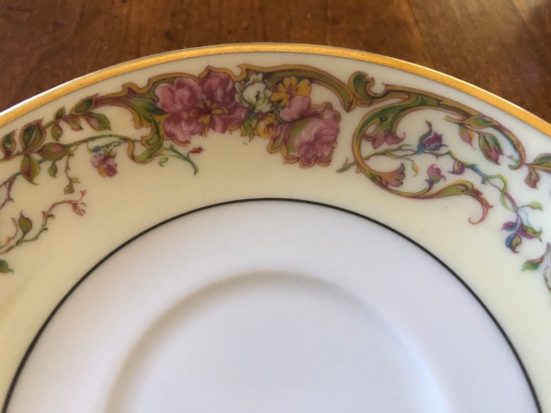 Puede incluir: Un platillo de porcelana blanca con un borde dorado y un dise&ntilde;o floral en tonos de rosa, verde y amarillo.