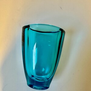 May include: A teal blue glass vase with a rounded bottom and a wide opening.