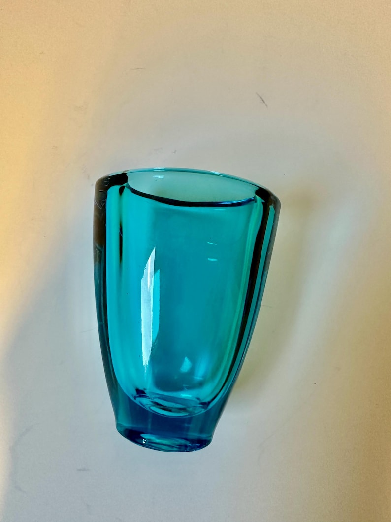 May include: A teal blue glass vase with a rounded bottom and a wide opening.