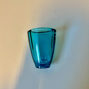 May include: A small, teal blue glass vase with a rounded, slightly flared opening.