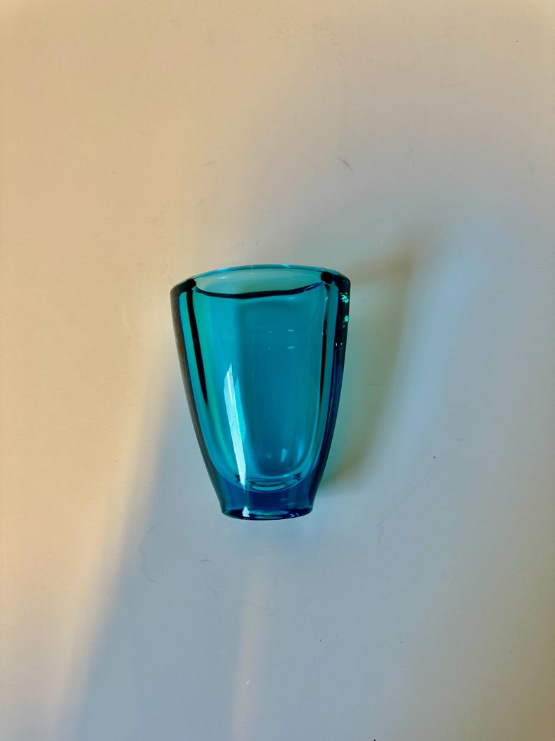 May include: A small, teal blue glass vase with a rounded, slightly flared opening.