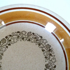 May include: A white ceramic plate with a brown and orange rim and a brown floral design around the centre.