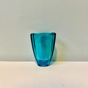 May include: A small, teal blue glass vase with a rounded, flared opening and a slightly wider base.