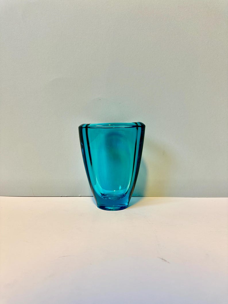 May include: A small, teal blue glass vase with a rounded, flared opening and a slightly wider base.