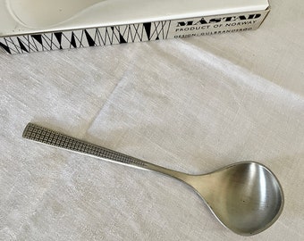 May include: A silver serving spoon with a patterned handle. The spoon is in a white box with the text "MASTAD PRODUCT OF NORWAY DESIGN GULLBRANDSEN".
