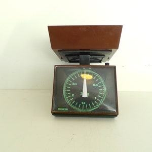 May include: A brown and black kitchen scale with a round, green dial. The dial has markings for 0.5, 1, 1.5, 2, 2.5, and 3. The scale is set to 0.