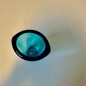 May include: A teal blue glass vase with a rounded, slightly oval shape. The vase has a dark blue rim.