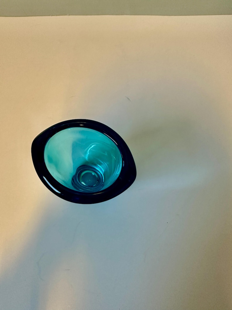 May include: A teal blue glass vase with a rounded, slightly oval shape. The vase has a dark blue rim.