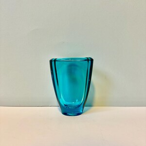 May include: A small, teal blue glass vase with a rounded, slightly flared opening and a slightly wider base.